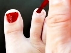 Red nail polish on toes. lady paints her toenails with red polish Regina Noir.